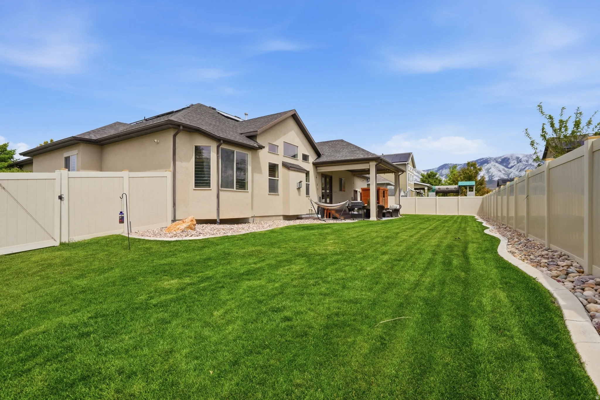 Expansive backyard featuring a manicured lawn, a covered patio, and a light-toned privacy fence