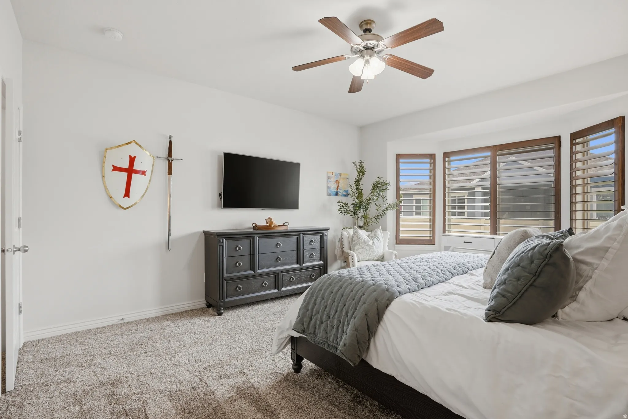 Master bedroom featuring a bay window with plantation shutters, ceiling fan with integrated lighting, and neutral carpeting