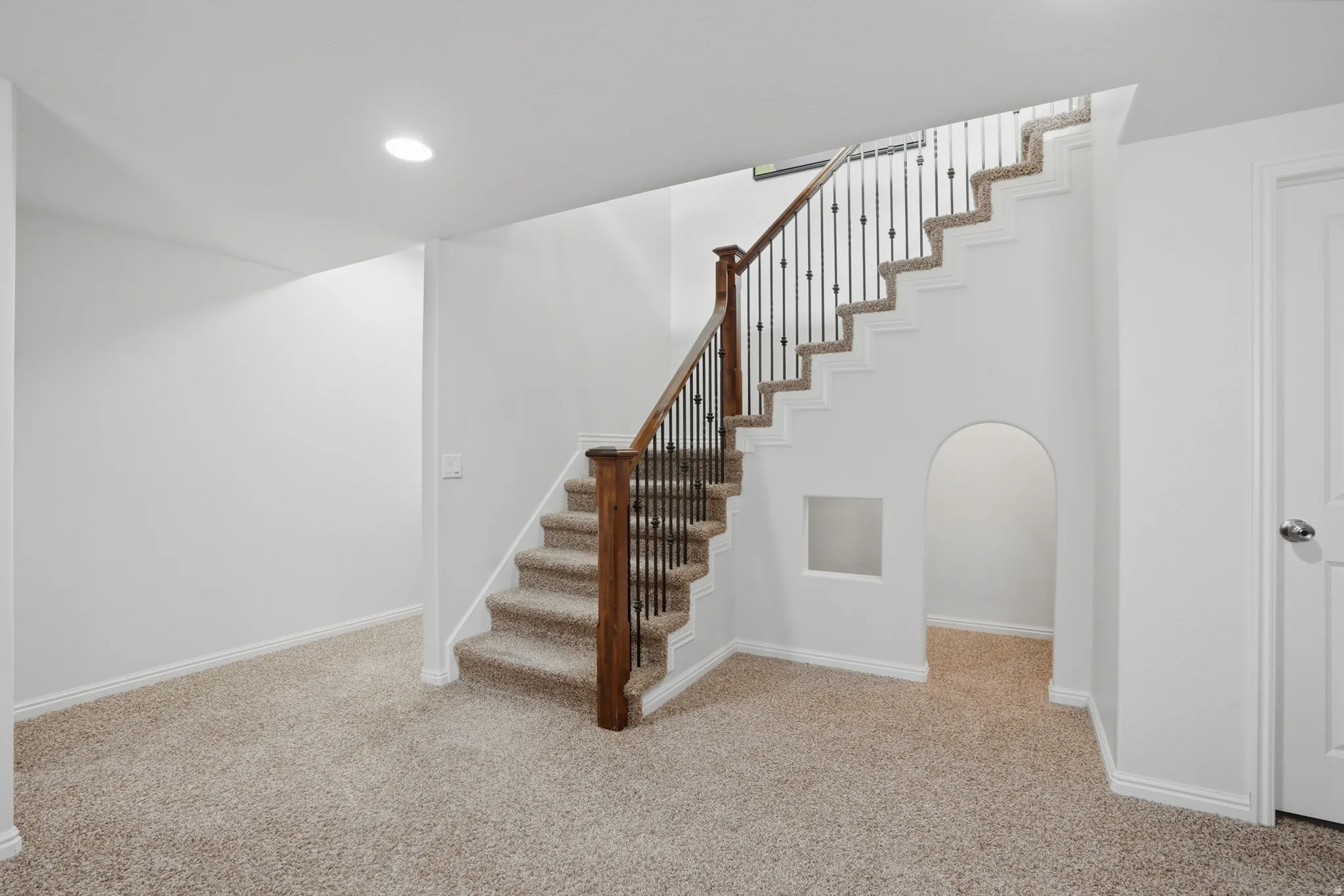 Carpeted staircase with dark wood newel posts and wrought iron balusters