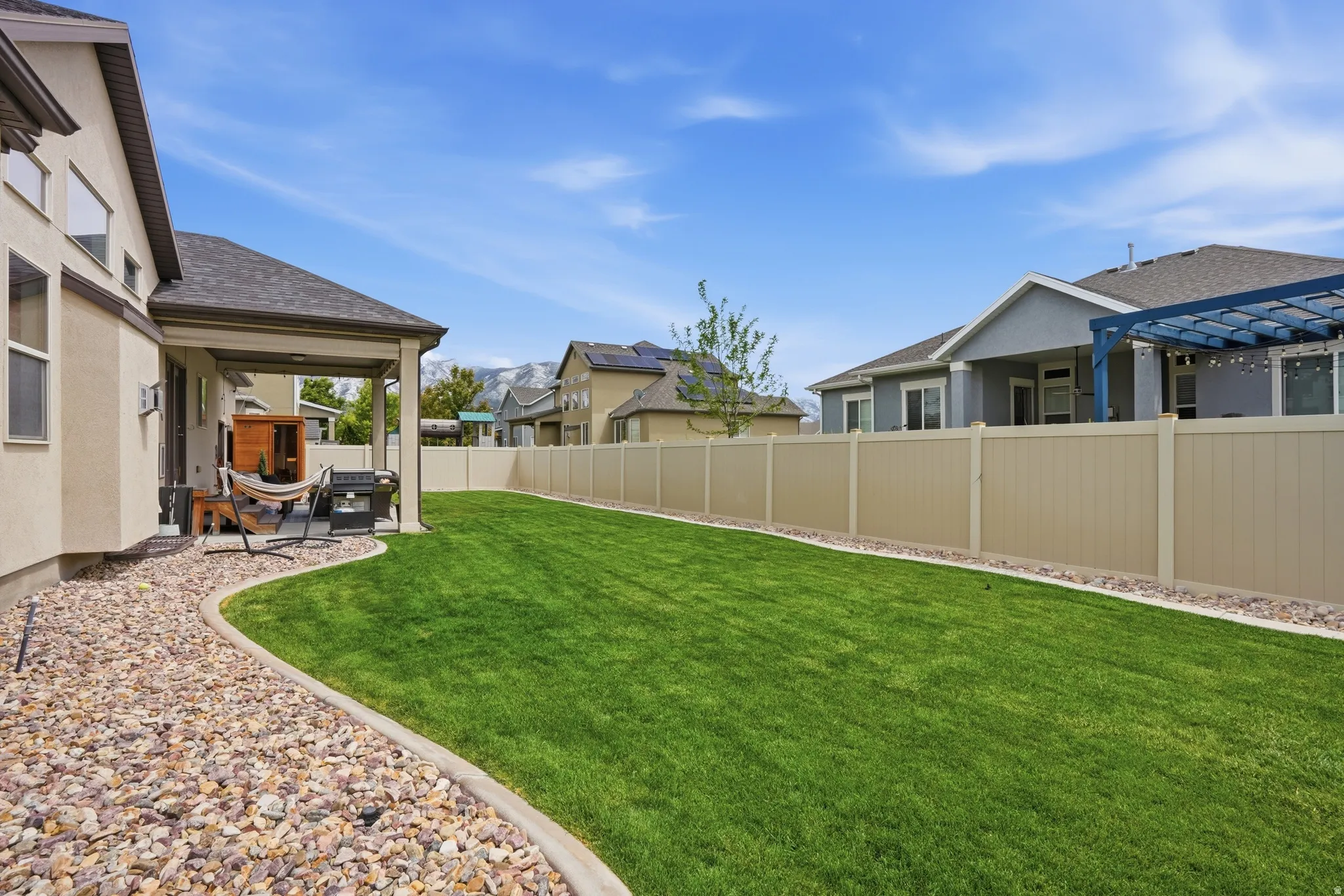 Expansive backyard featuring a manicured lawn, full fencing, and a covered patio area