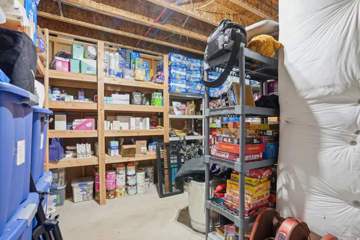Spacious storage area featuring exposed ceiling joists, concrete flooring, and multiple shelving units