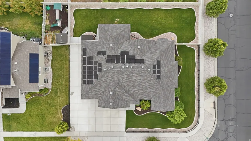 Aerial view of a residential property featuring a gray shingle roof, multiple solar panels, a concrete driveway, and a manicured lawn