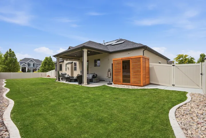 Spacious backyard featuring a manicured lawn, an outdoor sauna (optional), a covered patio, a concrete patio extension, and a privacy fence
