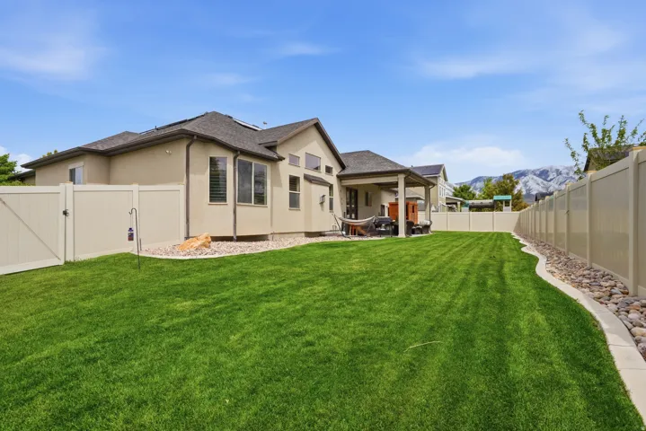Expansive backyard featuring a manicured lawn, a covered patio, and a light-toned privacy fence