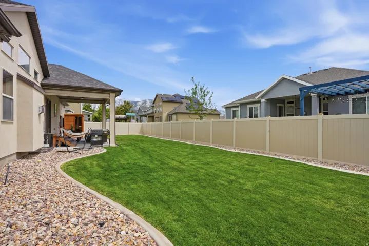 Expansive backyard featuring a manicured lawn, full fencing, and a covered patio area