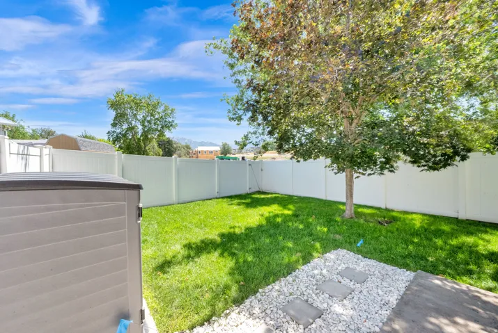 Expansive backyard featuring a manicured lawn, established tree, and full perimeter fencing