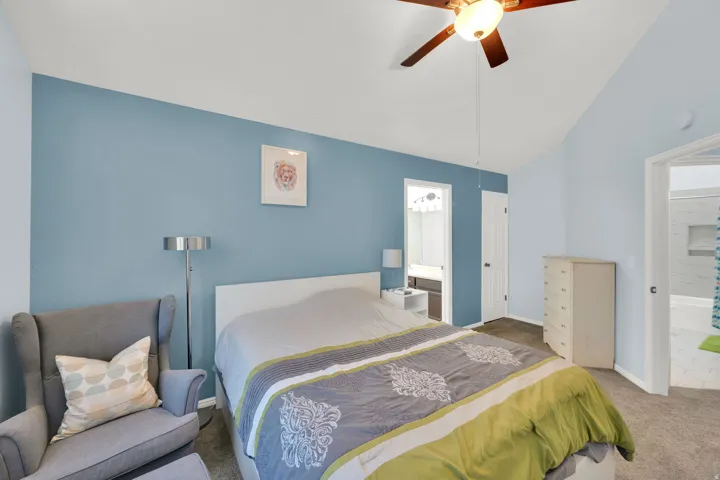 Vaulted ceiling with a ceiling fan, carpeted flooring, and a doorway to an adjacent bathroom featuring a vanity with a light fixture and mirror