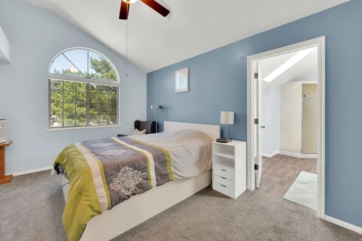 Vaulted ceiling bedroom featuring an arched window, ceiling fan, and carpet flooring