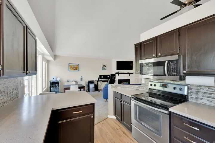 Kitchen featuring dark wood cabinetry, light-toned countertops, stainless steel appliances, and a mosaic tile backsplash