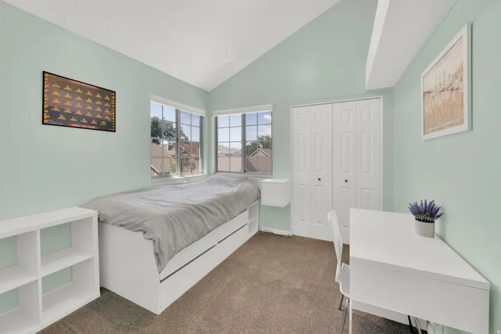 Vaulted ceiling bedroom featuring expansive windows, neutral-toned carpeting, and a bi-fold closet