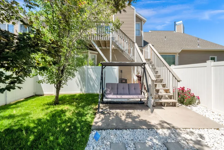 Private backyard featuring a manicured lawn, concrete patio, white vinyl fencing, and a mature tree