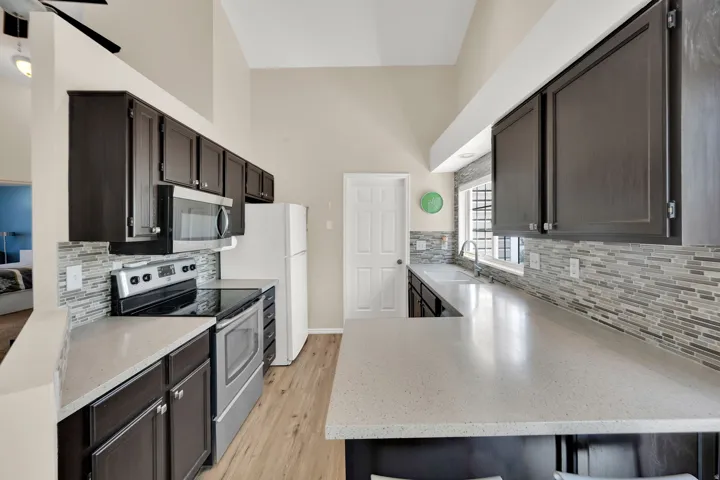 Kitchen featuring dark wood cabinetry, light-toned countertops, stainless steel appliances, a mosaic tile backsplash, and wood-finish flooring