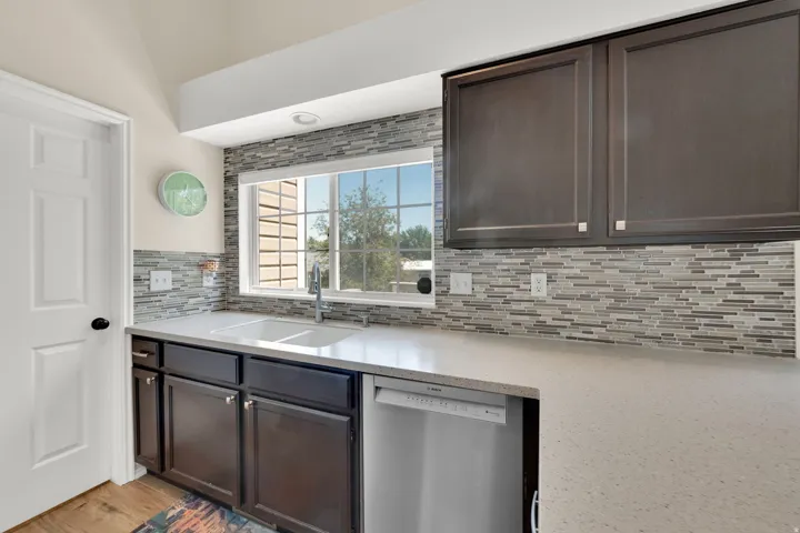 Kitchen featuring a double basin sink, dark wood-finish cabinetry, light-toned countertops, and a full-height mosaic tile backsplash