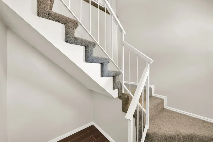 Staircase with carpeted treads and risers, white painted balusters, and a white handrail