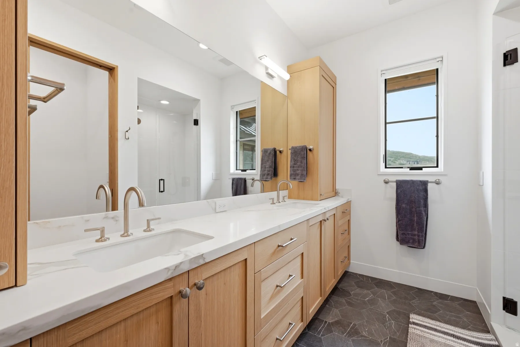 Double vanity featuring light wood cabinetry and a continuous white countertop with integrated sinks