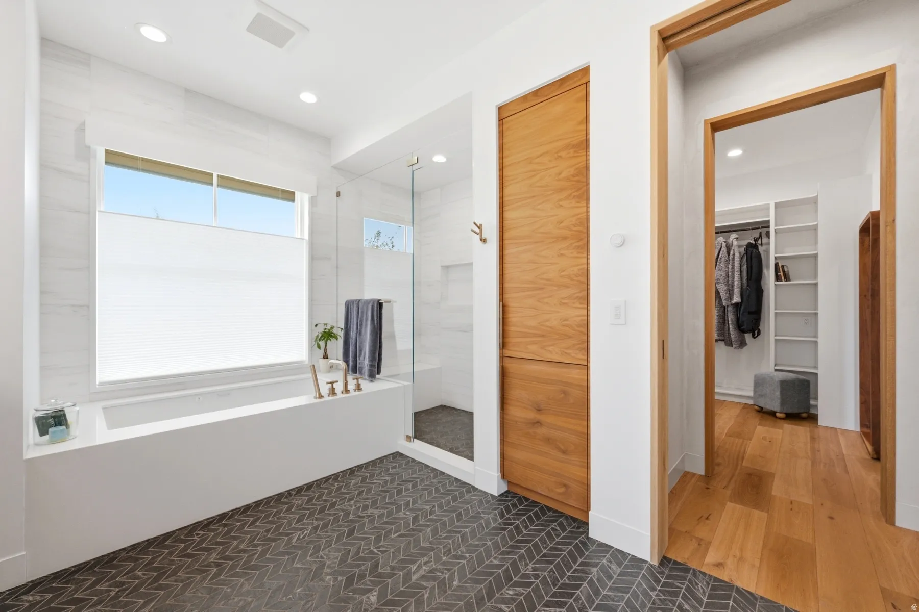 Contemporary bathroom featuring a built-in soaking tub with brass fixtures, a glass-enclosed shower, and herringbone-patterned floor tiles