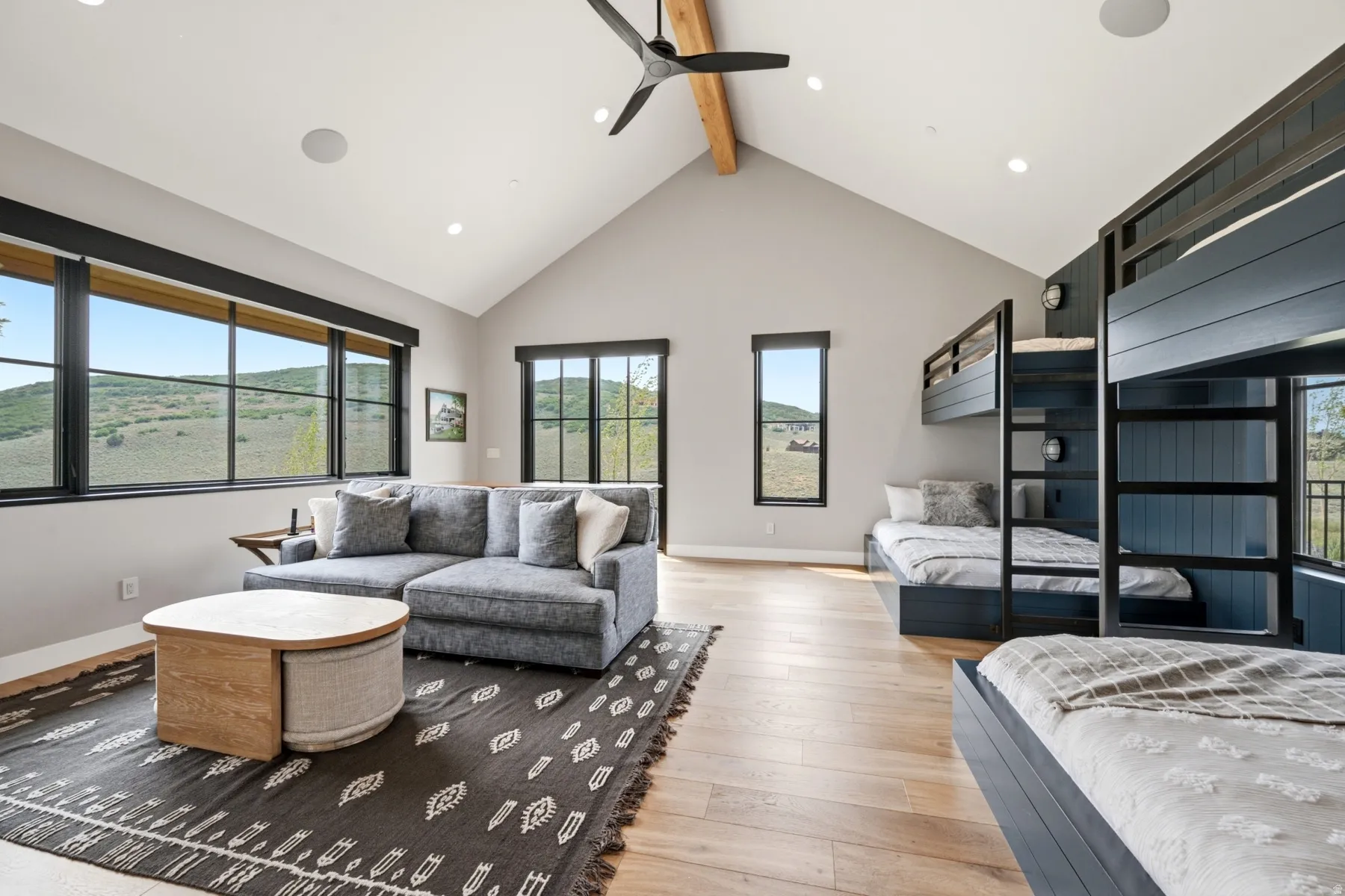 Spacious room featuring vaulted ceilings with exposed wood beams, expansive windows, multiple built-in bunk beds, wood-finish flooring, and recessed lighting