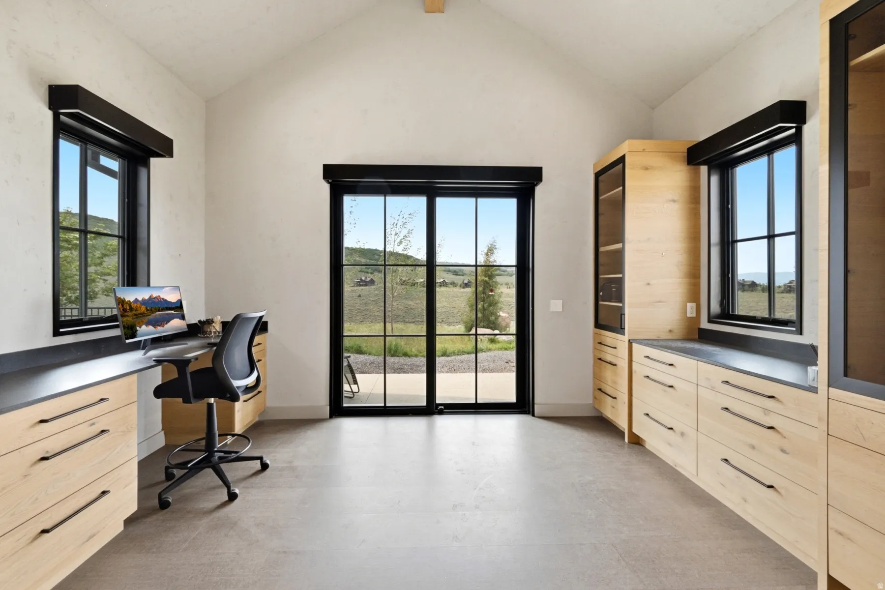 Vaulted ceiling room featuring light wood-finish cabinetry with dark hardware and countertops