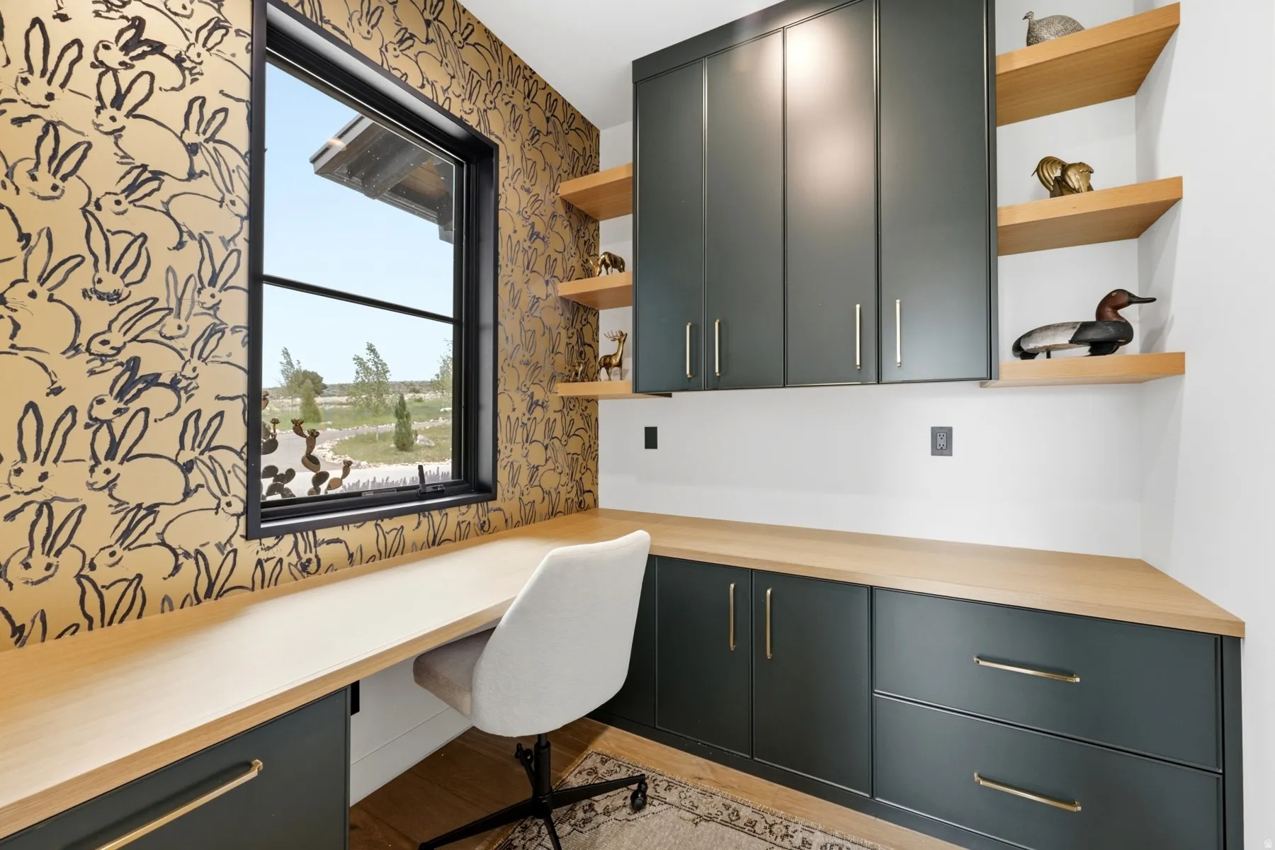Built-in desk area featuring ample cabinetry, natural wood-finish countertops, floating shelving, and a large black-framed window