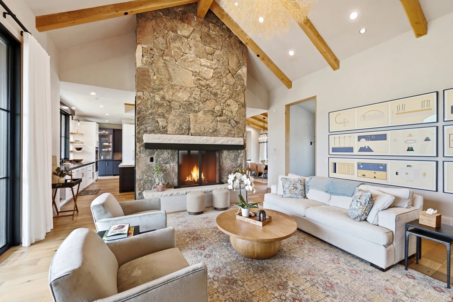 Vaulted ceiling with exposed wood beams, a prominent floor-to-ceiling stone fireplace, and light wood-finish flooring