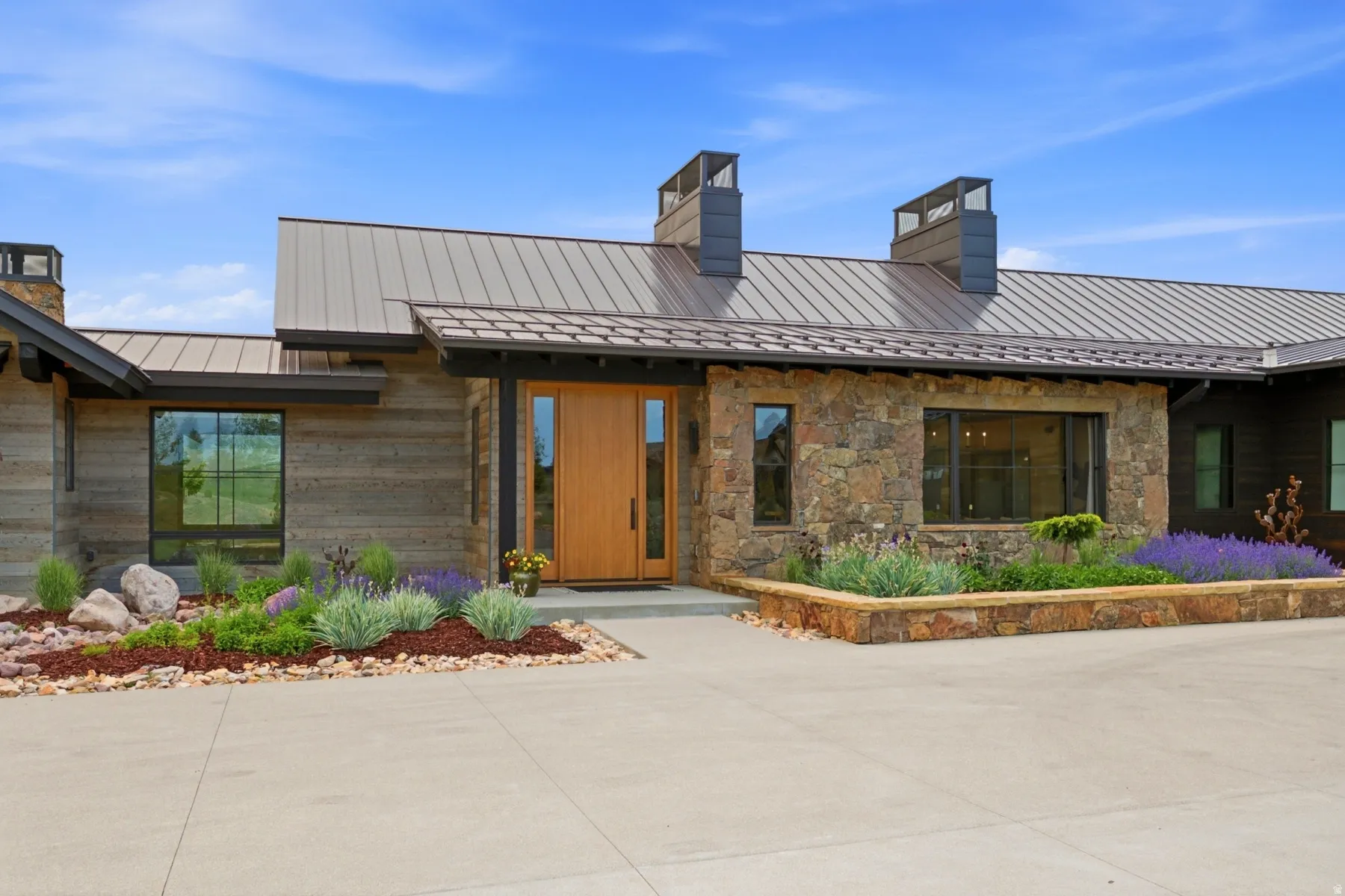 Contemporary exterior featuring a natural wood-finish door, stone accents, horizontal wood siding, a metal roof, and integrated landscaping with a stone planter box