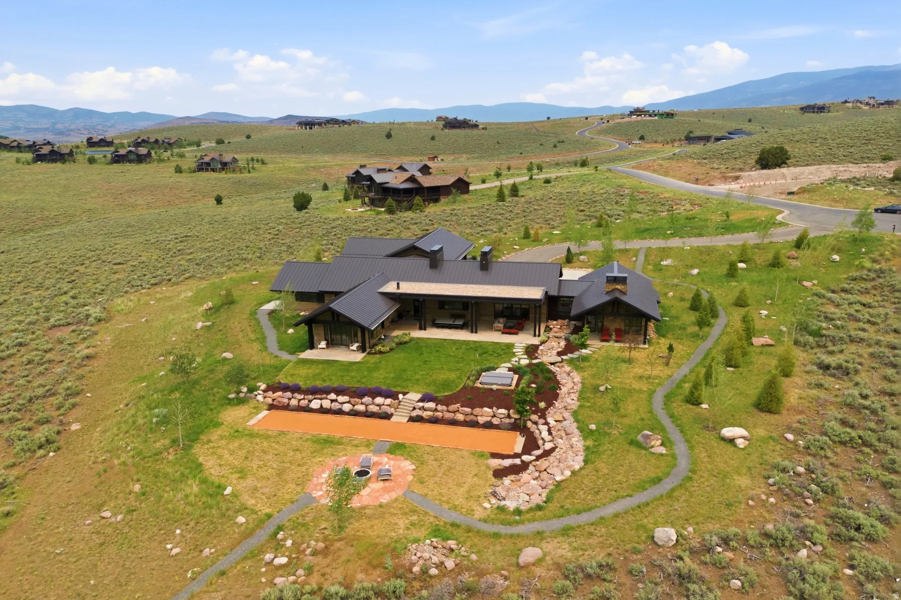 Modern mountain home featuring a dark metal roof, extensive outdoor patio, and a tiered landscaped backyard