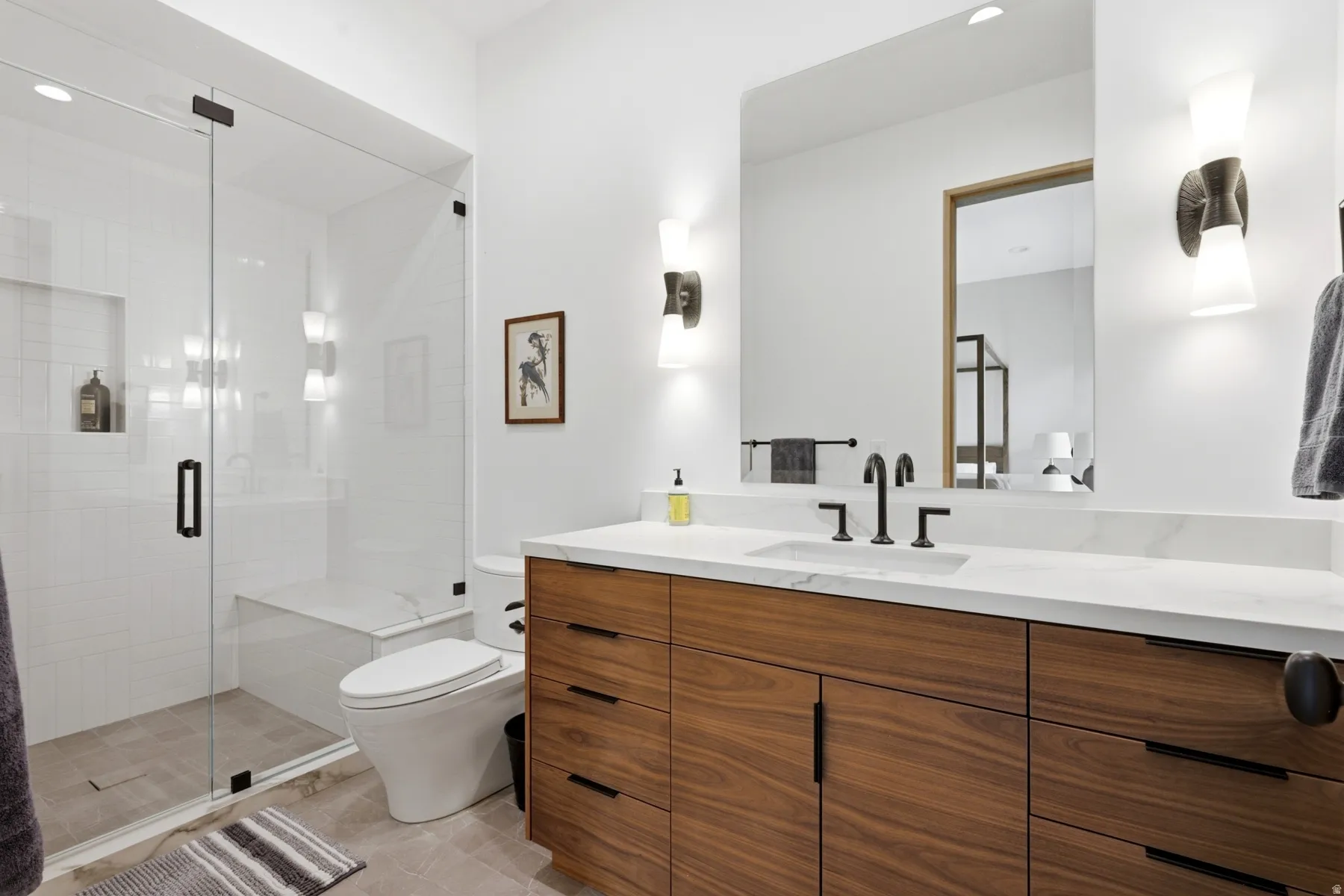Spacious bathroom featuring a frameless glass shower enclosure with a built-in bench, a large wood-finish vanity with ample storage, a white countertop, and a rectangular undermount sink with a matte black faucet