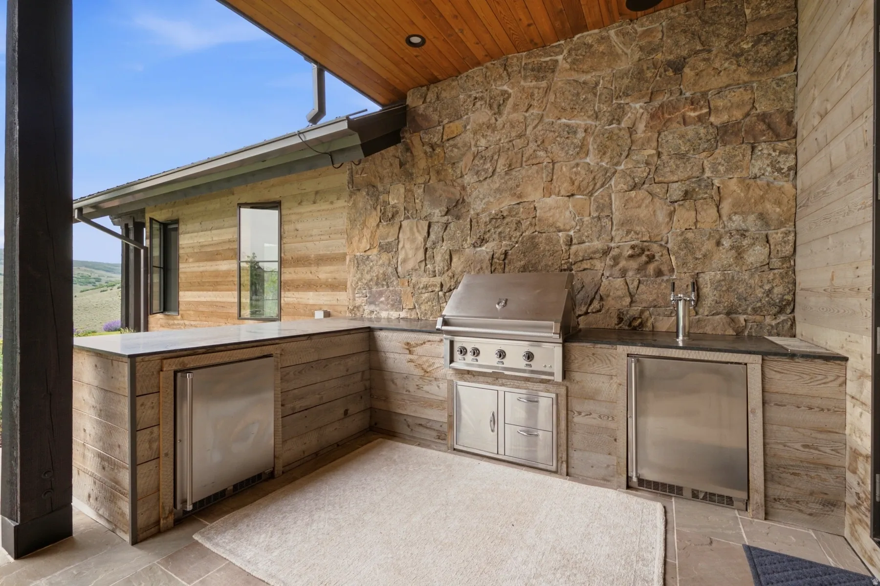 Outdoor kitchen featuring a built-in stainless steel grill, beverage refrigerator, and tap system