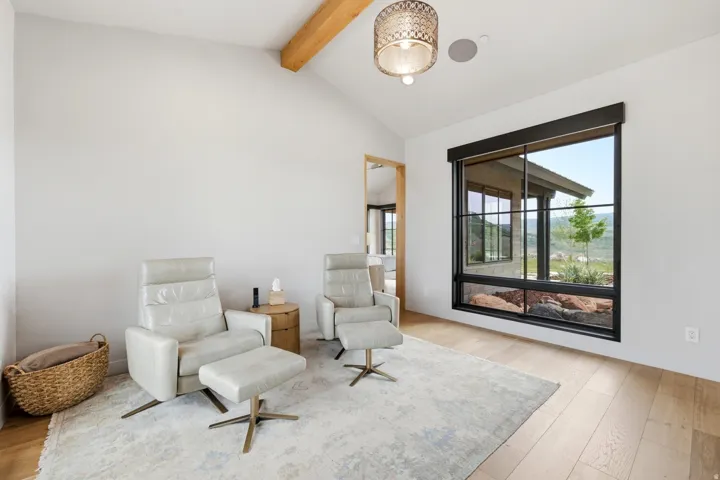 Spacious room featuring a vaulted ceiling with a visible wood beam, a large multi-pane window with black framing, and light wood-finish flooring