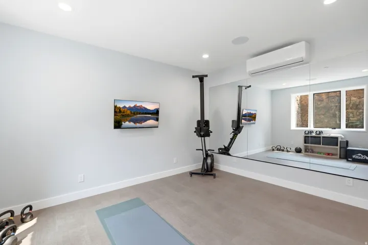 Dedicated fitness space featuring wall-mounted television, full-height mirrored wall, recessed lighting, and individual climate control