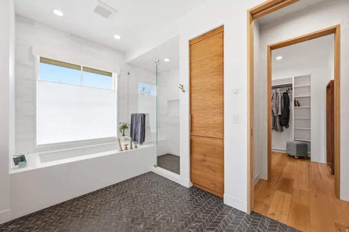 Contemporary bathroom featuring a built-in soaking tub with brass fixtures, a glass-enclosed shower, and herringbone-patterned floor tiles