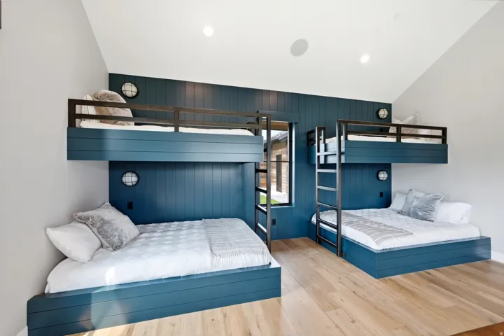 Room featuring four built-in bunk beds with slatted blue bases and metal frames, a shiplap accent wall, light wood-finish flooring, and a vaulted ceiling with recessed lighting