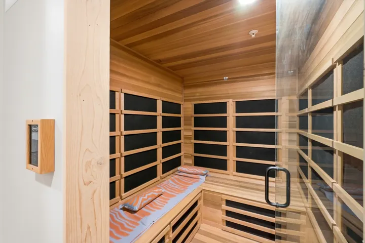 Wood-paneled sauna featuring a glass entry door with a metal pull handle, slatted wood benches, and built-in heat elements