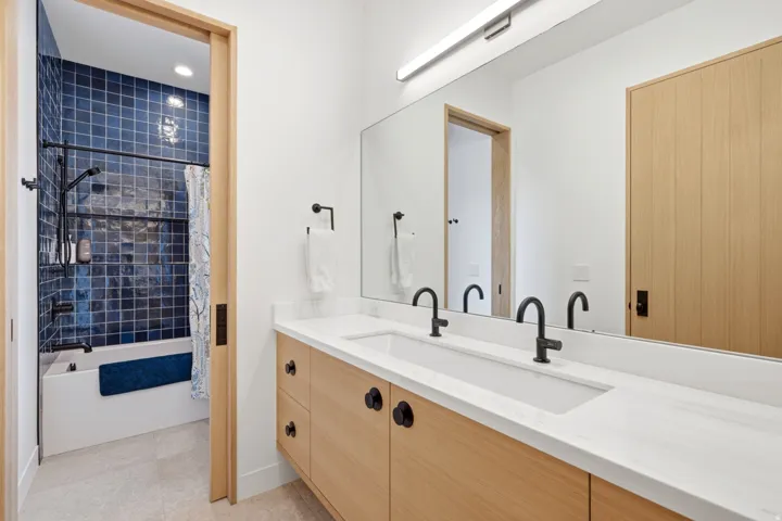 Dual vanity with integrated sinks and white countertops, light wood-finish cabinetry, and matte black hardware