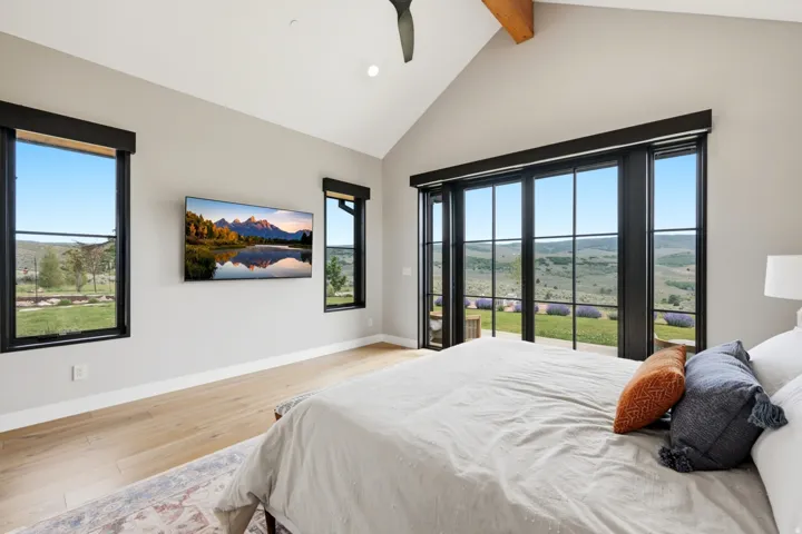 Vaulted ceiling room featuring light wood-finish flooring and multiple black-framed windows