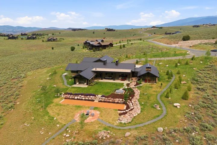 Modern mountain home featuring a dark metal roof, extensive outdoor patio, and a tiered landscaped backyard