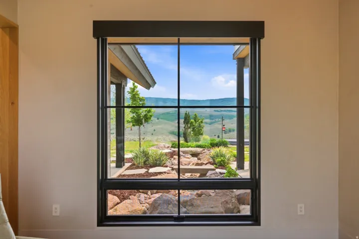 Expansive window with black grid framing a landscaped outdoor area and distant hills