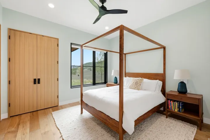 Bedroom featuring wood-finish flooring, light-toned walls, and a black ceiling fan