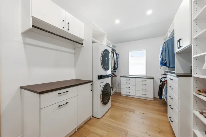 Spacious utility room featuring integrated laundry appliances, custom white cabinetry with dark countertops, built-in shelving, and wood-finish flooring