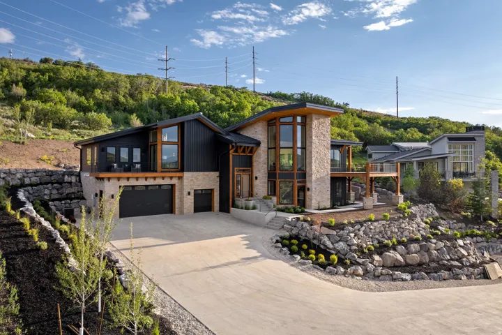 Modern hillside residence featuring a stone and vertical siding exterior, expansive windows, a two-car garage, and terraced landscaping with rock retaining walls