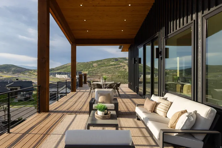 Expansive outdoor deck featuring wood-finish decking, a solid wood-beamed overhead structure with recessed lighting, and black metal railings