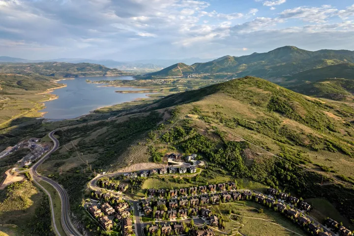 Aerial landscape featuring a large body of water, expansive green hills, and a residential development