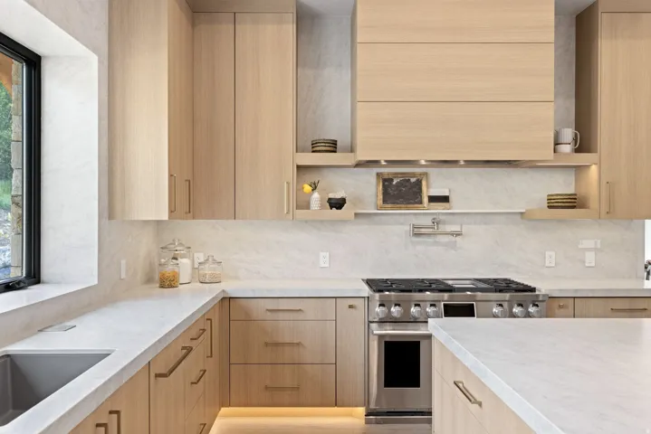 Contemporary kitchen featuring light wood-finish cabinetry, light-toned countertops, a stainless steel range with overhead ventilation, and an undermount sink