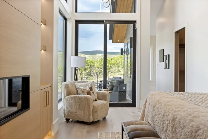 Floor-to-ceiling windows with expansive outdoor views, light wood-finish flooring, built-in cabinetry with integrated lighting, and a modern fireplace insert