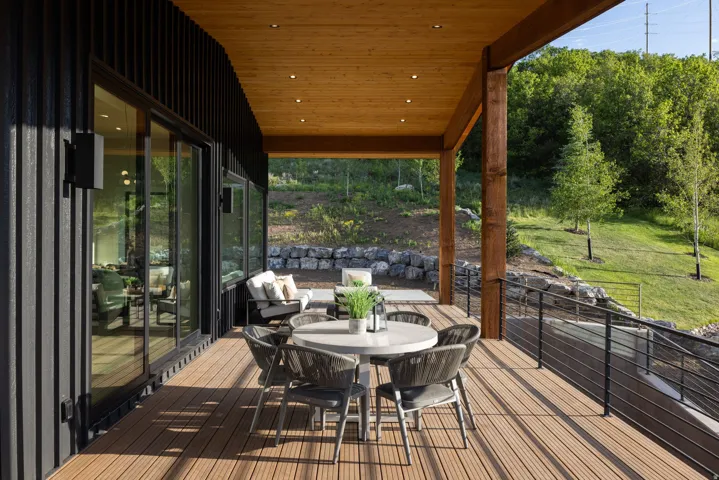 Expansive outdoor deck featuring composite decking, a wood-paneled ceiling with recessed lighting, and a modern black cable railing