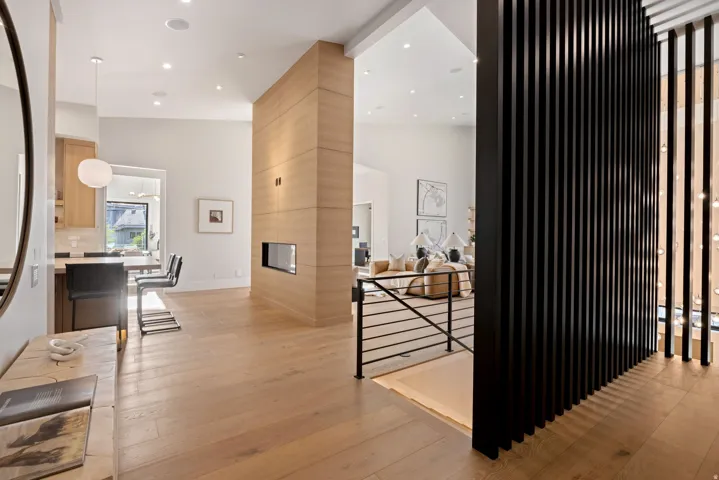 Open-concept interior featuring light wood-finish flooring, a modern gas fireplace with a wood-paneled surround, and a black slatted room divider