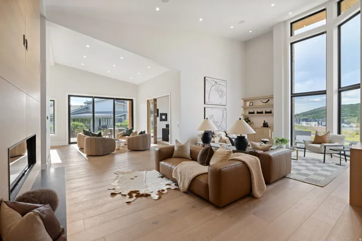 Spacious living area featuring high vaulted ceilings, expansive floor-to-ceiling windows, wood-finish flooring, a built-in fireplace, and sliding glass doors