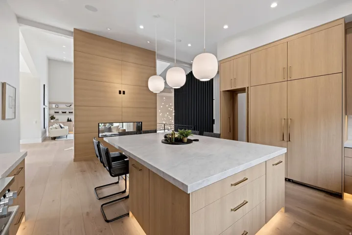 Spacious kitchen featuring a large island with a light-toned countertop, integrated appliances, extensive wood-finish cabinetry, and recessed lighting