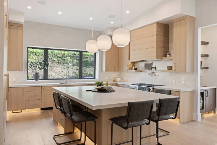 Kitchen featuring a spacious island with seating, integrated cooktop with custom hood, light wood-finish cabinetry, and a large horizontal window