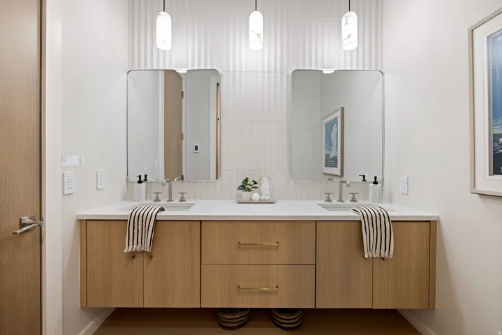 Dual vanity featuring a white countertop, two undermount sinks with brushed nickel fixtures, and light wood-finish cabinetry with brass hardware